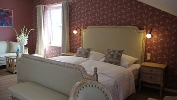A bedroom with a large bed, two bedside tables, a nightstand, a bench, and a window with curtains.
