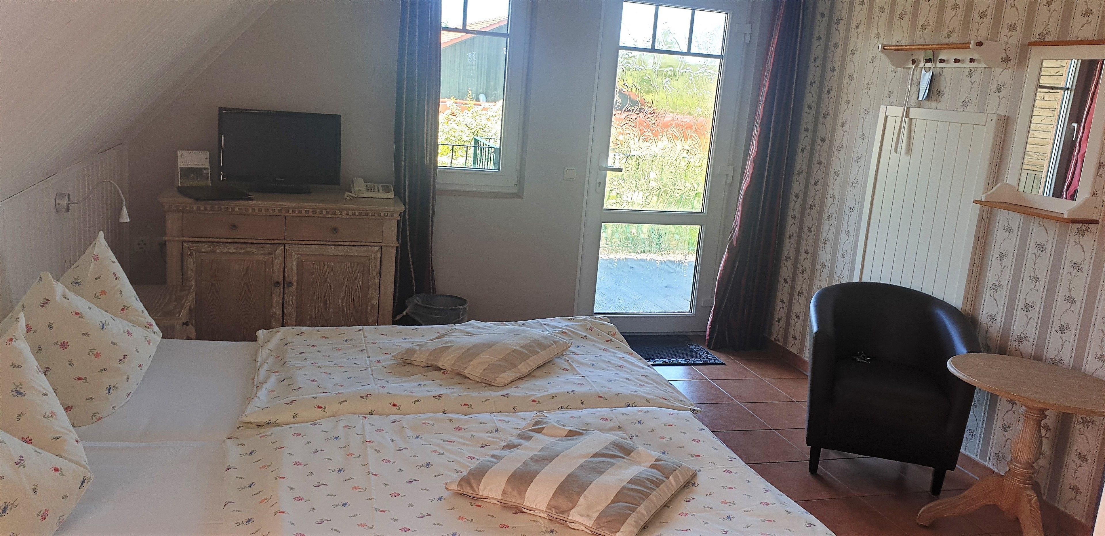 A bedroom with a bed, a TV on a dresser, a chair, and a window with a view of greenery.