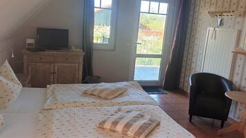 A bedroom with a bed, a TV on a dresser, a chair, and a window with a view of greenery.
