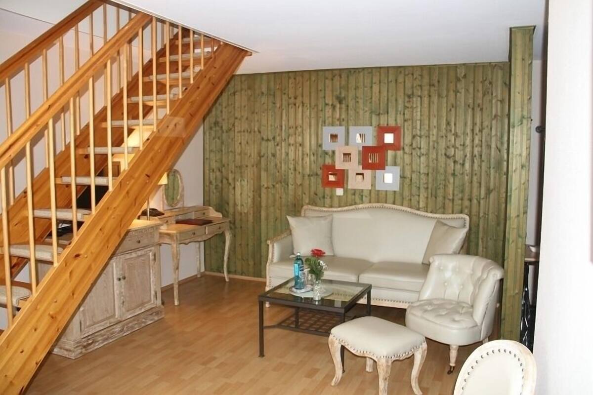 A living room with a wooden staircase, a white sofa, a glass coffee table, and a wall with framed pictures.