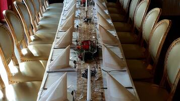 Una larga mesa de comedor dispuesta para un evento formal, con manteles blancos, cubertería ordenada y cristalería.