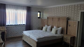 A bedroom with a wooden bed, a desk, a chair, a wardrobe, and a window with curtains.