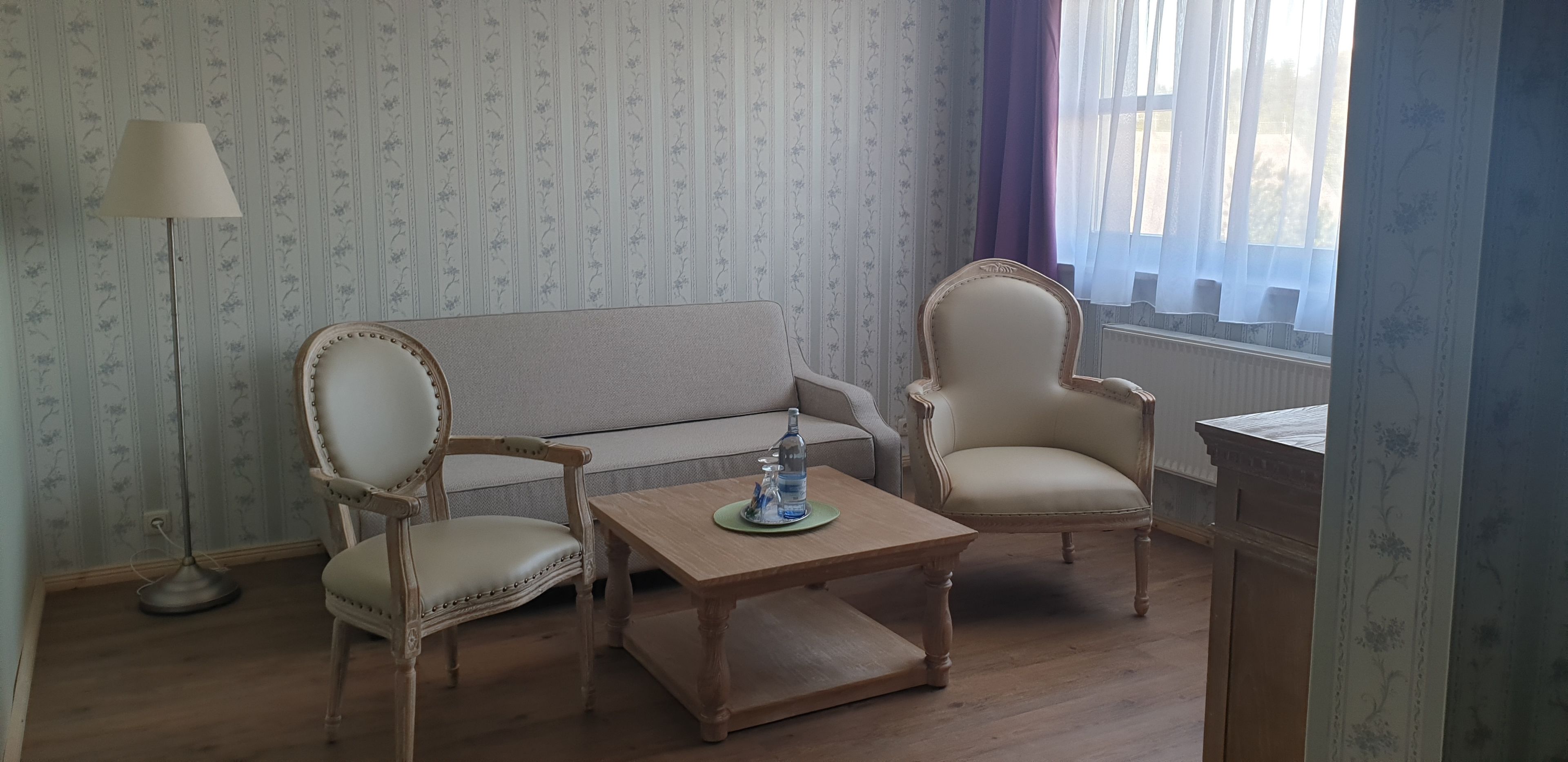 Una habitación con un sofá, dos sillones, una mesita de madera y una lámpara de pie.