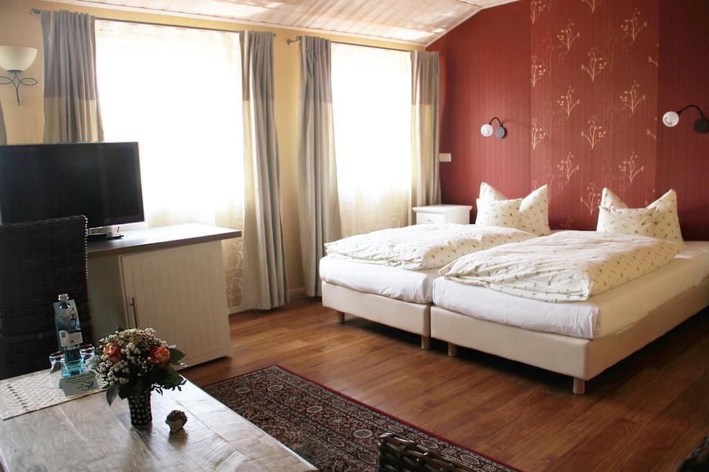 A bedroom with a bed, a desk with a TV, a nightstand, a lamp, and a window with curtains.