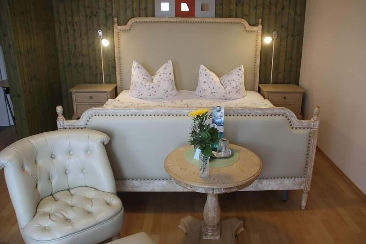 A bedroom with a bed, two bedside tables, a chair, and a small round table with a vase of flowers.