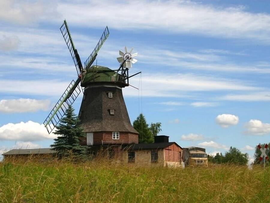 Un molino tradicional con un reloj en la parte superior, rodeado de edificios y un campo cubierto de hierba.