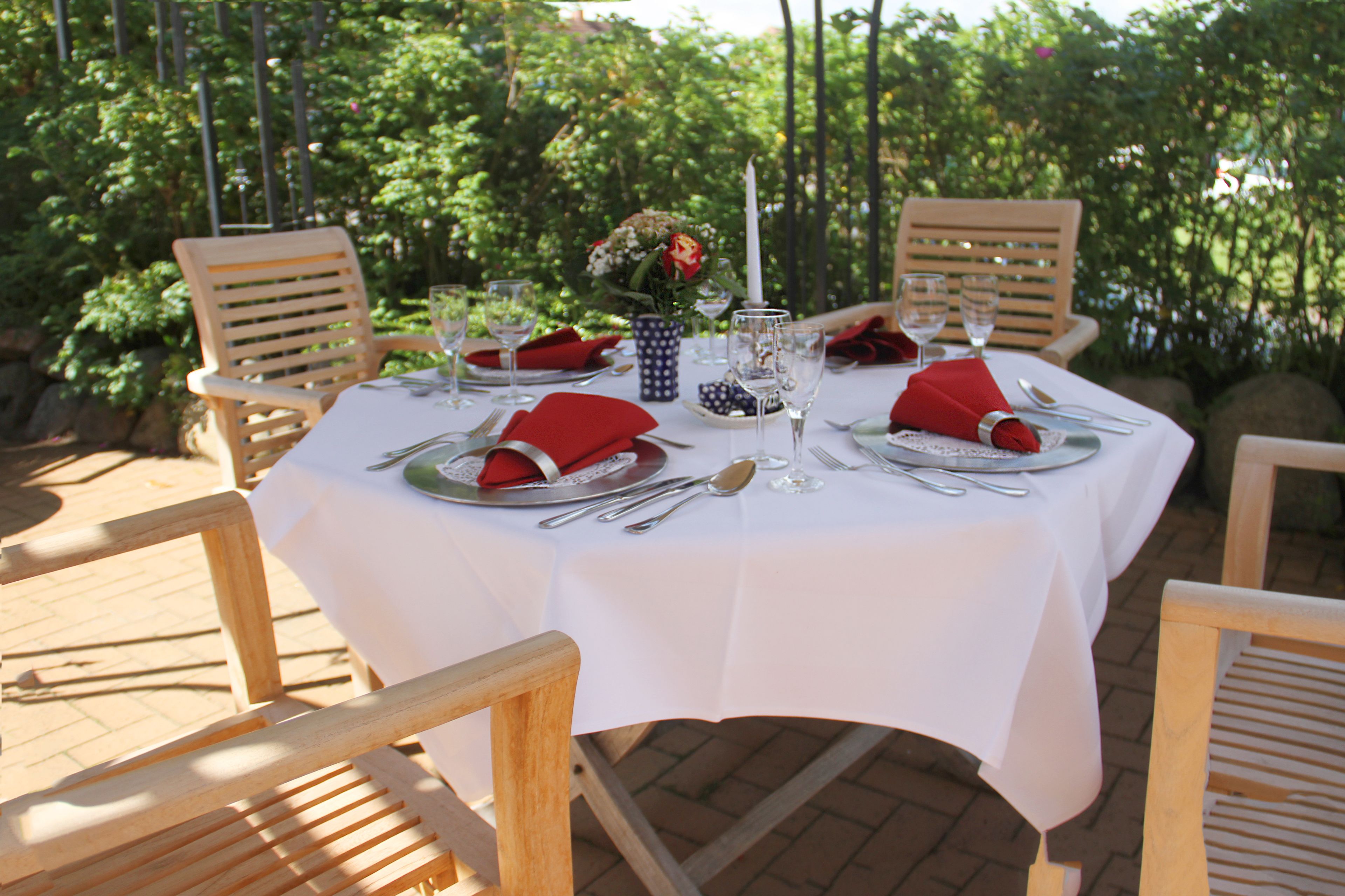 A table set for four with white tablecloths, wooden chairs, and red napkins.