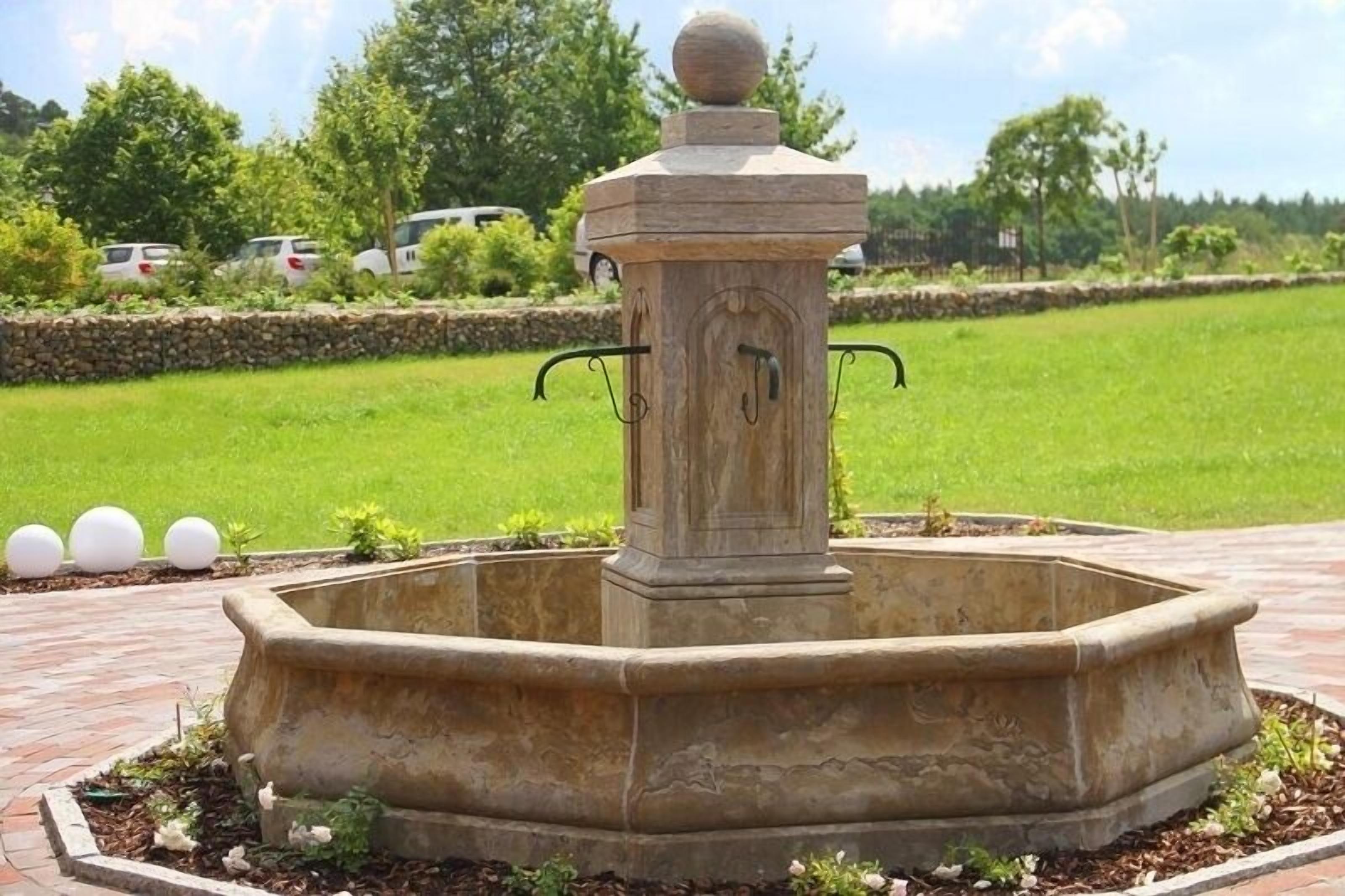 A stone fountain with a spherical top, surrounded by a brick border and small plants.