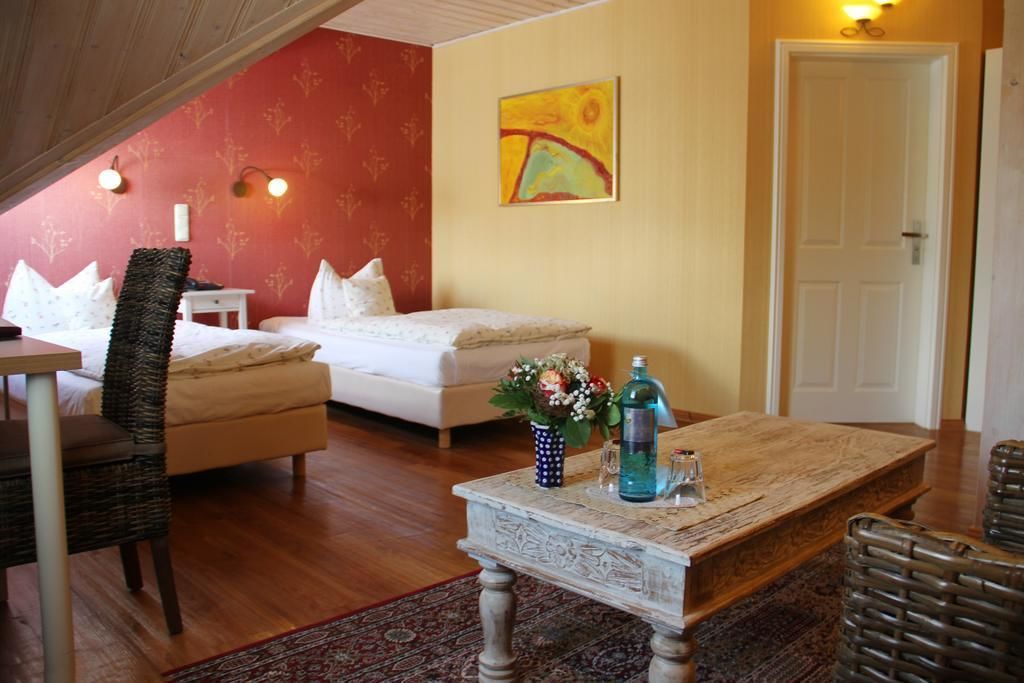 A cozy room with a bed, a dining table, and a chair. There is a door and a wall with a painting.