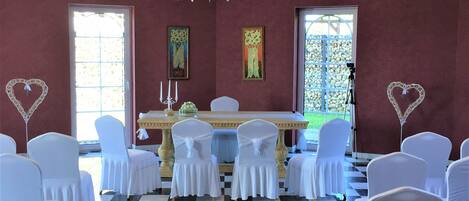 A room with a checkered floor, white chairs, a chandelier, and framed artwork on the walls.