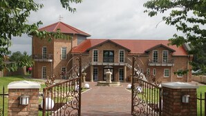 A large brick house with a red roof, a central entrance with a fountain, and a gated driveway. - Kur- & Landhotel Borstel-Treff (Dabel)