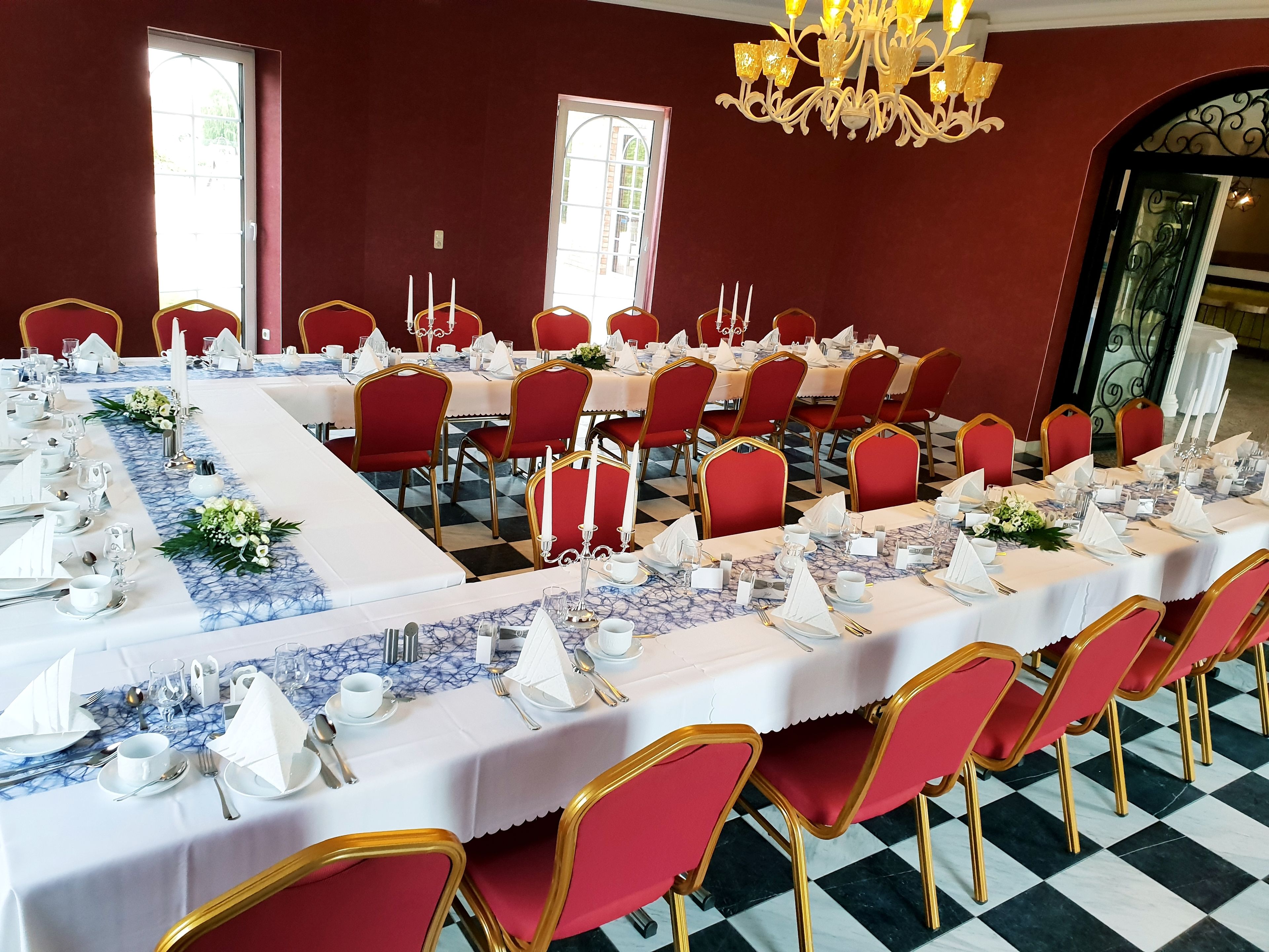 A banquet hall with long tables set for a formal event, featuring red chairs and white tablecloths.