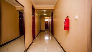 A hotel hallway with a fire extinguisher mounted on the wall, doors on both sides, and a tiled floor. - Nyaholoti Airport Hotel (Dar es Salaam)