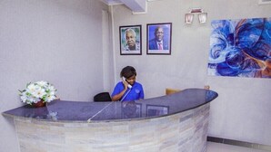 A reception desk with a glass top, a vase of white flowers, and framed pictures on the wall. - Nyaholoti Airport Hotel (Dar es Salaam)
