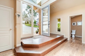 Een modern interieur met een houten vloer, een trap die naar een deur leidt, en uitzicht op buiten.