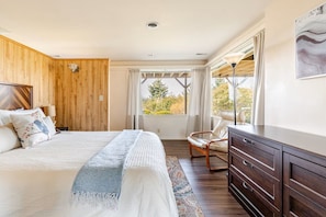 Ein Schlafzimmer mit einem Bett, einem Sessel, einer Kommode und einem Fenster mit Vorhängen.