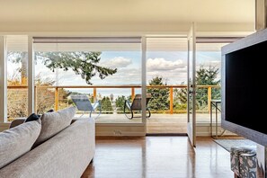 Ein modernes Wohnzimmer mit einer Couch, einem Flachbildfernseher und einem Balkon mit Blick auf Himmel und Bäume.