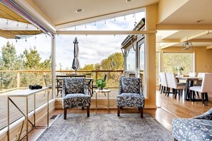 Een ruim balkon met een eethoek, twee stoelen, een tafel en uitzicht op bomen.