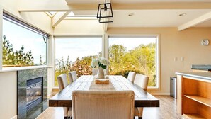 A dining area with a long table, chairs, a vase of flowers, and a view of trees through large windows. - Pritchard's Perch - private 2.5 acre in-city property, views from every room! (Seattle)
