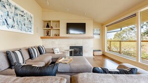 A modern living room with a sectional sofa, a flat-screen TV, a fireplace, and a large window with a view. - Pritchard's Perch - private 2.5 acre in-city property, views from every room! (Seattle)