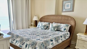 A wicker bed with a quilted cover, a bedside table with a lamp, and a framed picture on the wall.