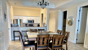 A dining area with a wooden table and chairs, a kitchen with white cabinets and appliances, and a chandelier.