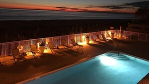A nighttime pool area with lounge chairs and a view of the ocean.