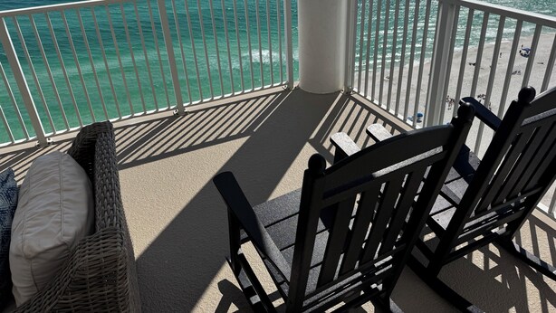 A balcony with a view of the ocean, wicker furniture, and a white railing.