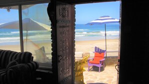 Uitzicht op een strand door een raam, met een strandstoel en parasol voor het raam.
