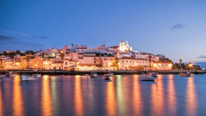 Un pueblo costero al anochecer, con edificios iluminados y barcos en el agua.
