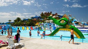 Zona de piscina con una gran decoración de dragón, toboganes acuáticos y sillas de descanso.