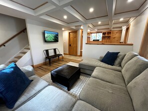 A living room with a sofa, ottoman, and a television mounted on the wall. - Private Home Walk to Okemo Lifts! Hot Tub/Fire Pit (Ludlow)