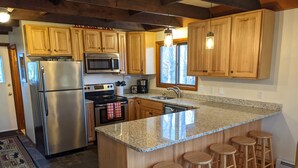 Una cocina con armarios de madera, electrodomésticos de acero inoxidable, encimera de granito y taburetes de bar.