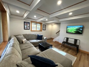 A living room with a sectional sofa, a flat-screen TV, and a window with a view.
