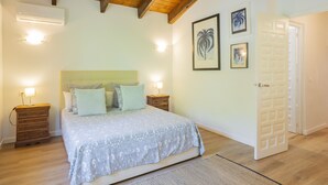 Camera da letto con un letto, travi in legno, condizionatore d'aria, comodino, cassettiera e quadri appesi al muro.