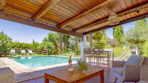 Un'area esterna riparata con piscina, sedie a sdraio, un tavolo in legno e un divano.