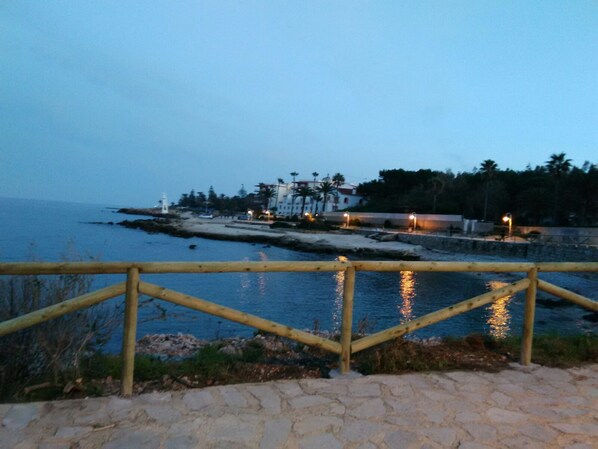 A coastal view with a wooden fence, a stone pathway, and a building with lights in the background. - EXCLUSIVE APARTMENT NEXT TO THE BEACH OF DENIA WIFI AND A/A (Denia)