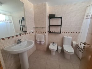 Ein Badezimmer mit Waschbecken, zwei Toiletten, einem Spiegel und einem Handtuchhalter.