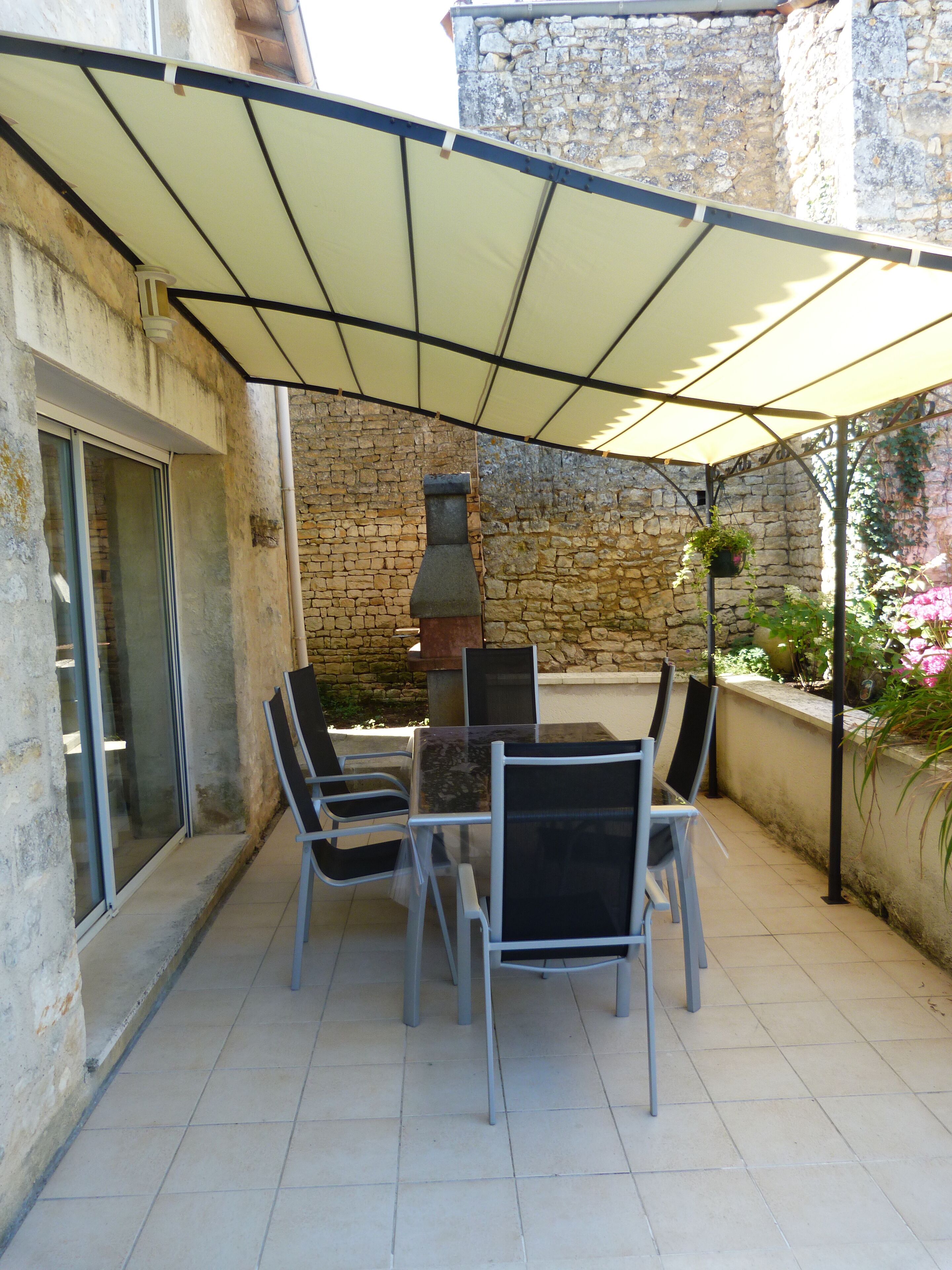 An outdoor patio with a stone wall, a grill, and a table with chairs.
