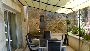 Eine Terrasse im Freien mit einer Steinsäule, einem Grill und einem Tisch mit Stühlen.