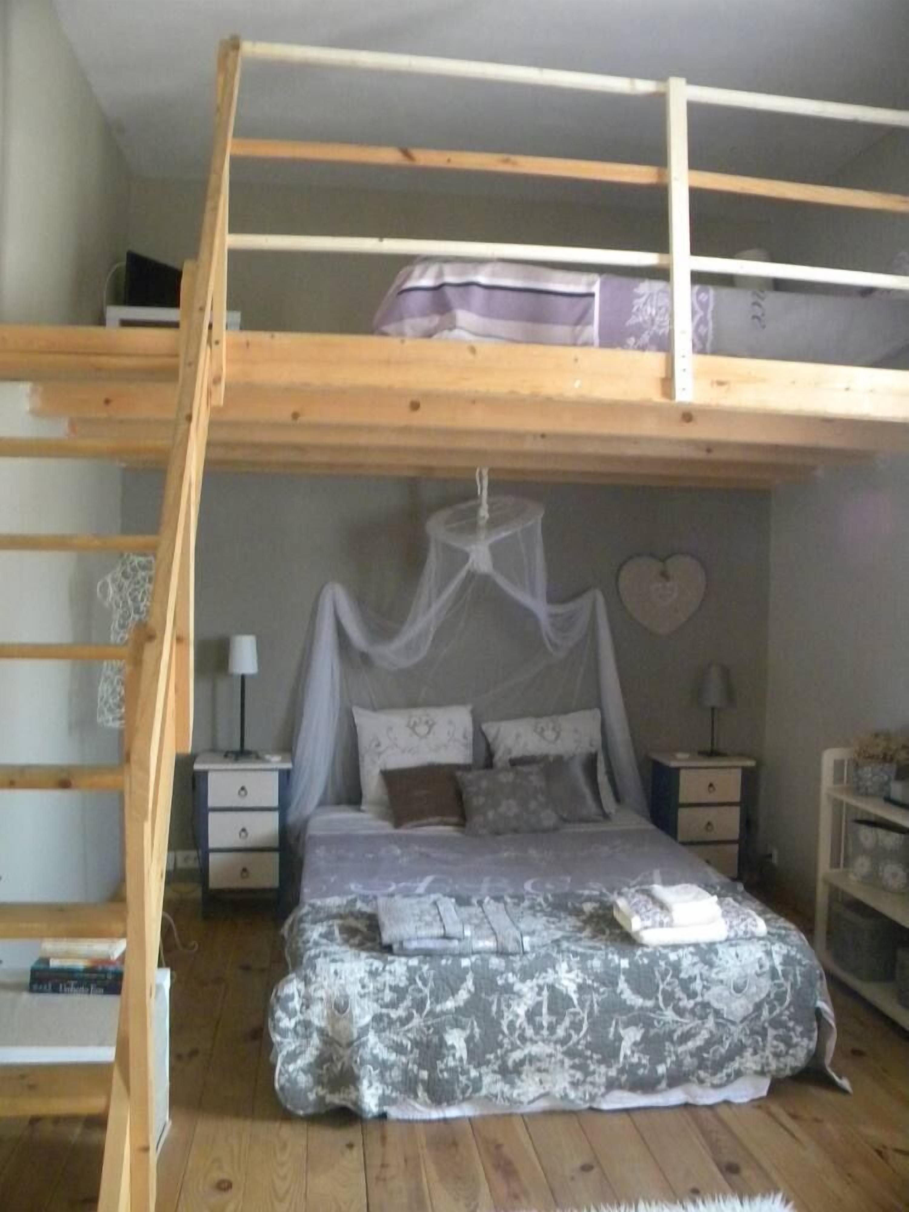 A bunk bed room with a wooden ladder, a canopy bed, bedside tables, and a small shelf.