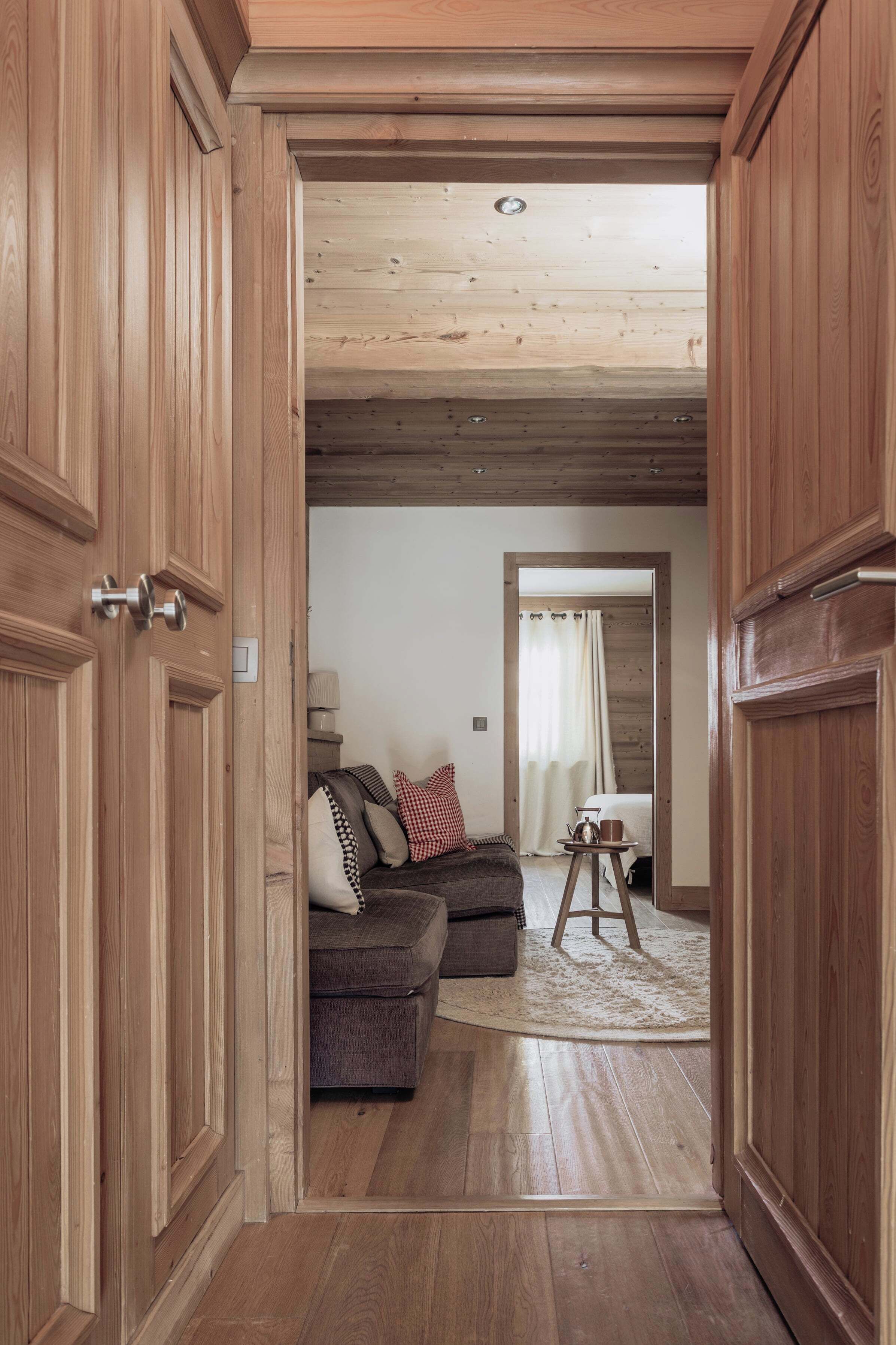 A wooden door leading to a living room with a sofa, a small table, and a lamp.