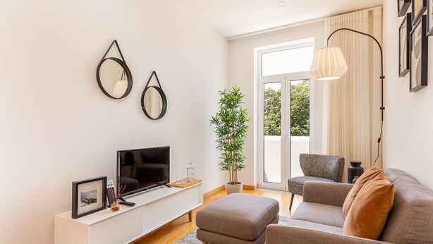 A modern living room with a flat-screen TV, a white console table, a grey sofa, and a potted plant.