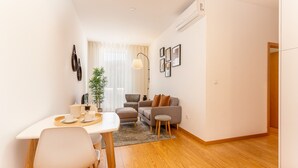 A modern living room with a sofa, armchair, and coffee table. There is a dining table with chairs and a small plant.