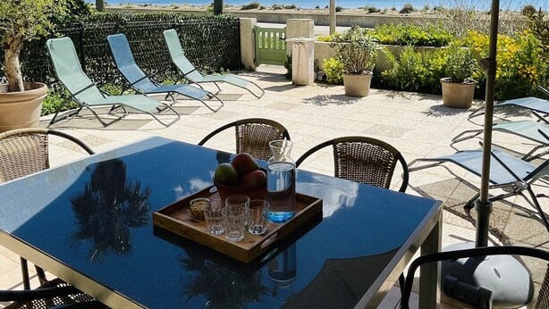 A patio with a table, chairs, and an umbrella overlooking a beach. - Generous exclusive holiday home in a dream location right on the beach with great views (Gruissan)