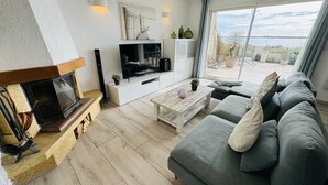 A modern living room with a fireplace, a flat-screen TV, a sofa, and a view of the outdoors. - Generous exclusive holiday home in a dream location right on the beach with great views (Gruissan)