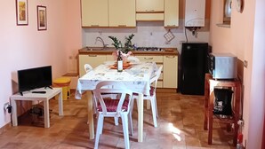 Una cocina compacta con una mesa de comedor, sillas, un televisor y un refrigerador.