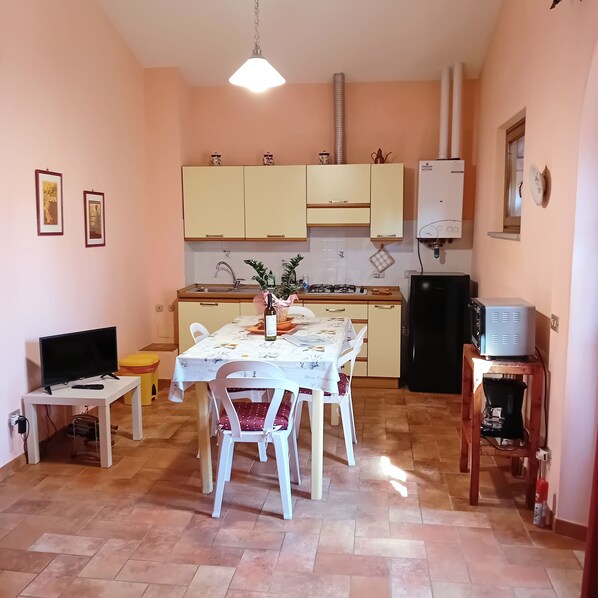 A compact kitchen with a dining table, chairs, a TV, and a refrigerator.