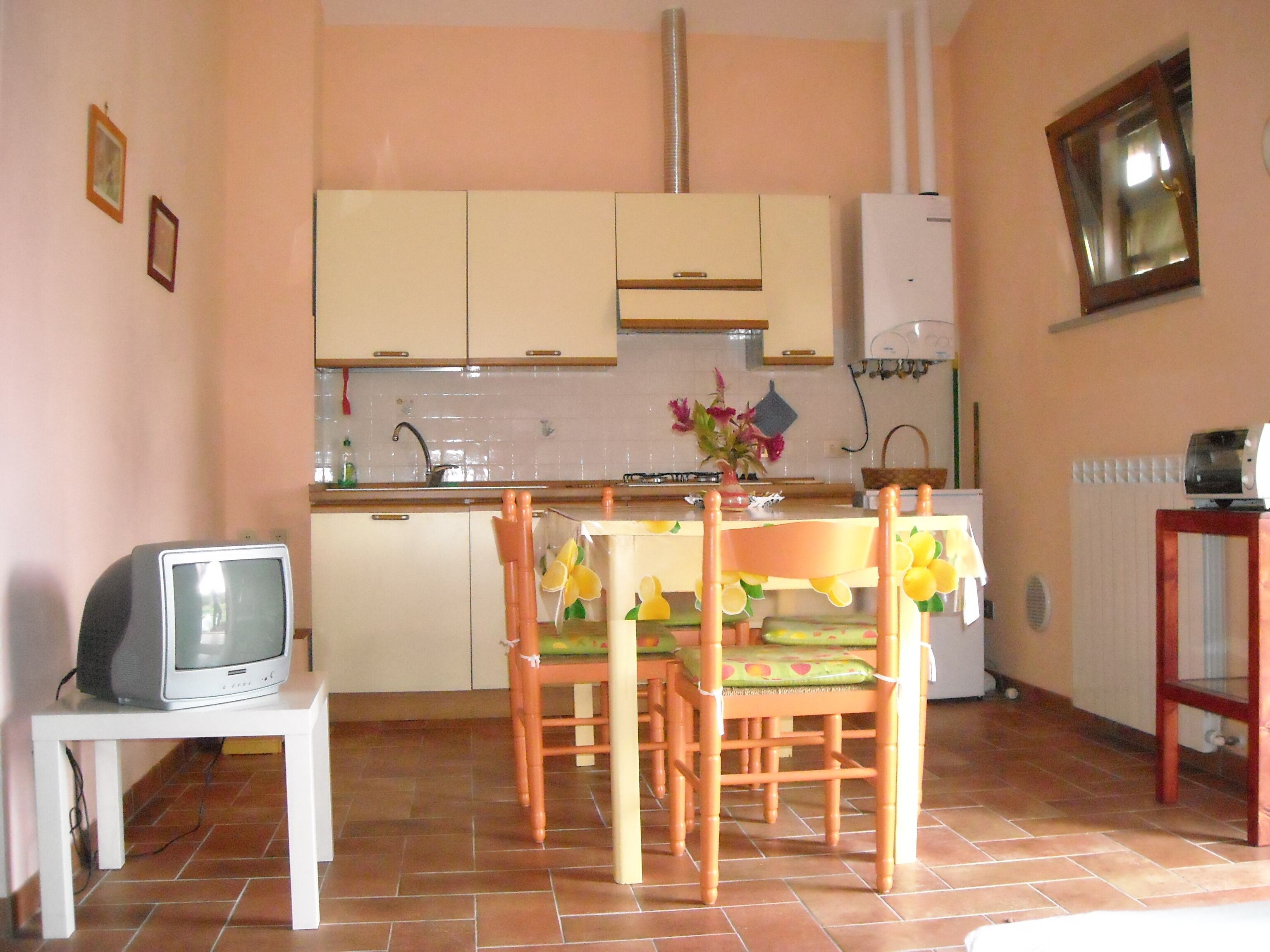 A small kitchen with white cabinets, a tiled backsplash, a dining table with chairs, and a television on a stand.