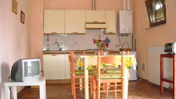 A small kitchen with white cabinets, a tiled backsplash, a dining table with chairs, and a television on a stand.